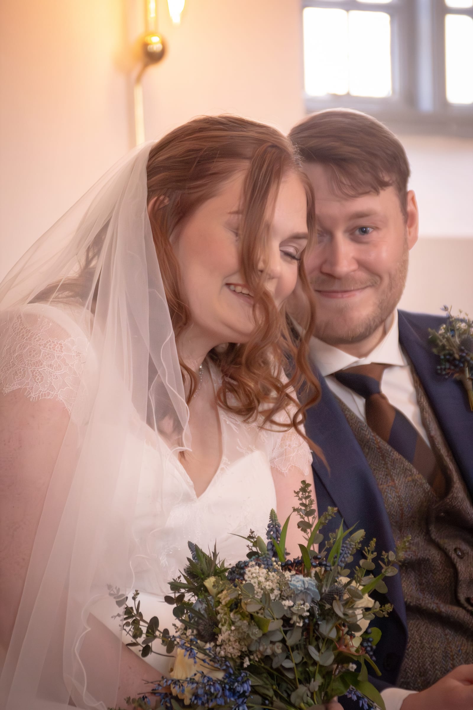 Brud og gom står tæt sammen og smiler med brudebuket i kirke