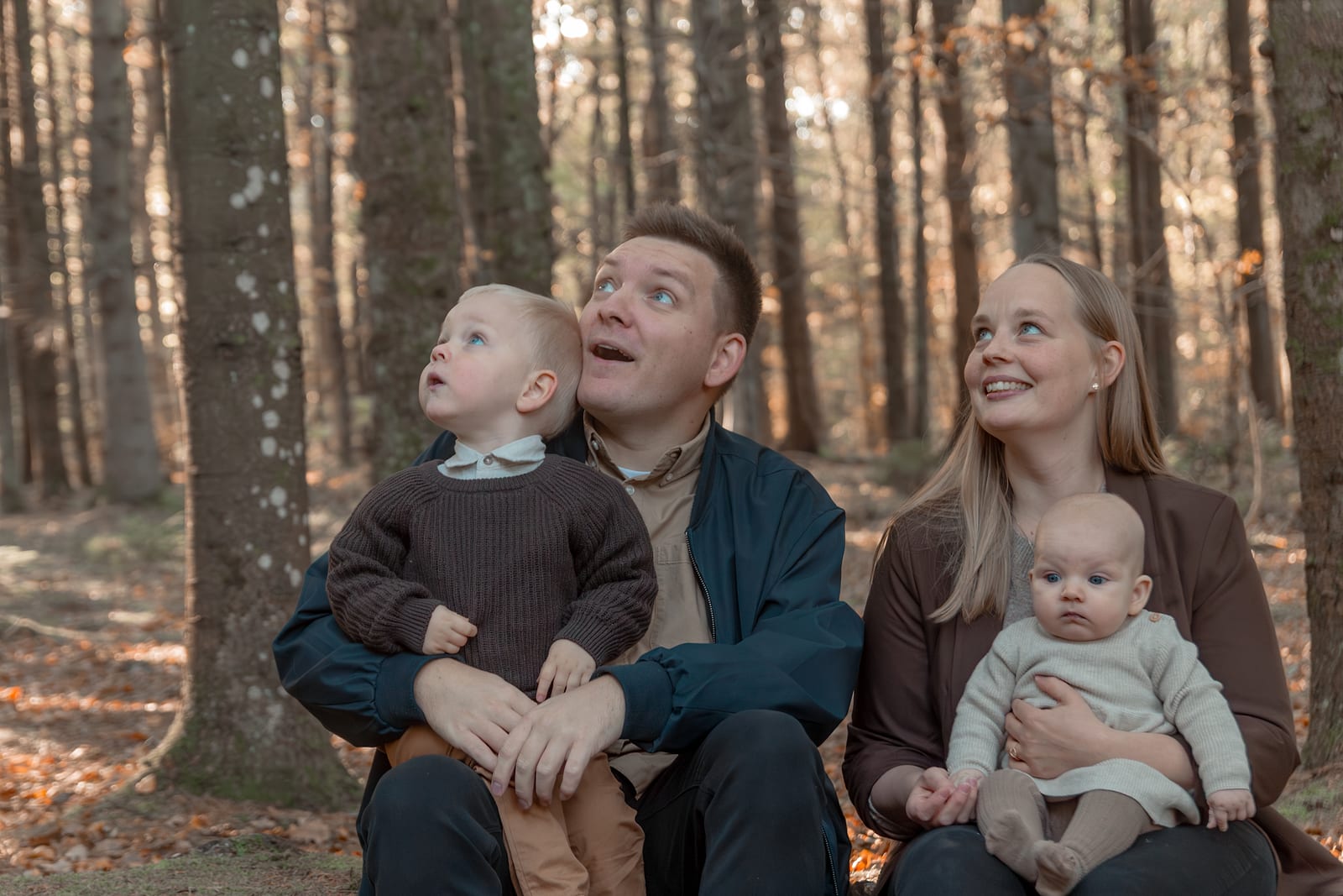 Familie med to børn smiler sammen i efterårsskov